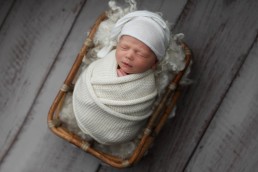 Capture the essence of a precious newborn in a white blanket, nestled in a basket on a wooden floor - perfect for newborn photography in Essex.