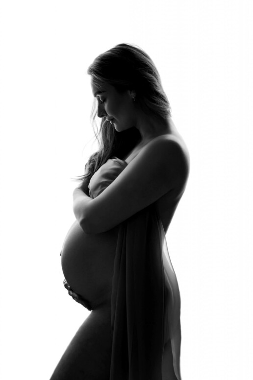 A pregnant woman is posing in front of a white background.