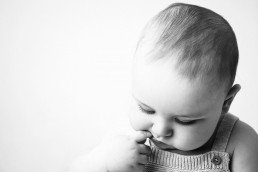 A black and white photo of a baby with his finger in his mouth.