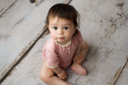 A baby girl sitting on a wooden floor.