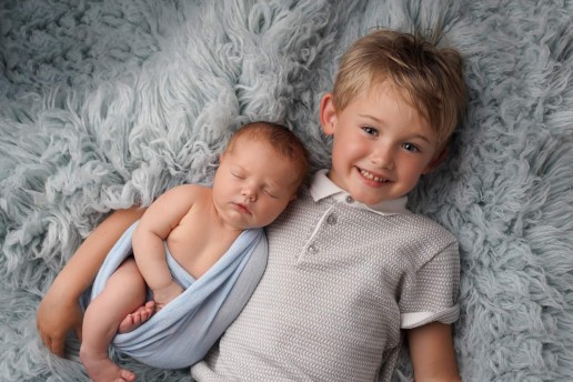 Two boys laying on a blue blanket.