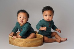 Two babies sitting in a wooden bowl.