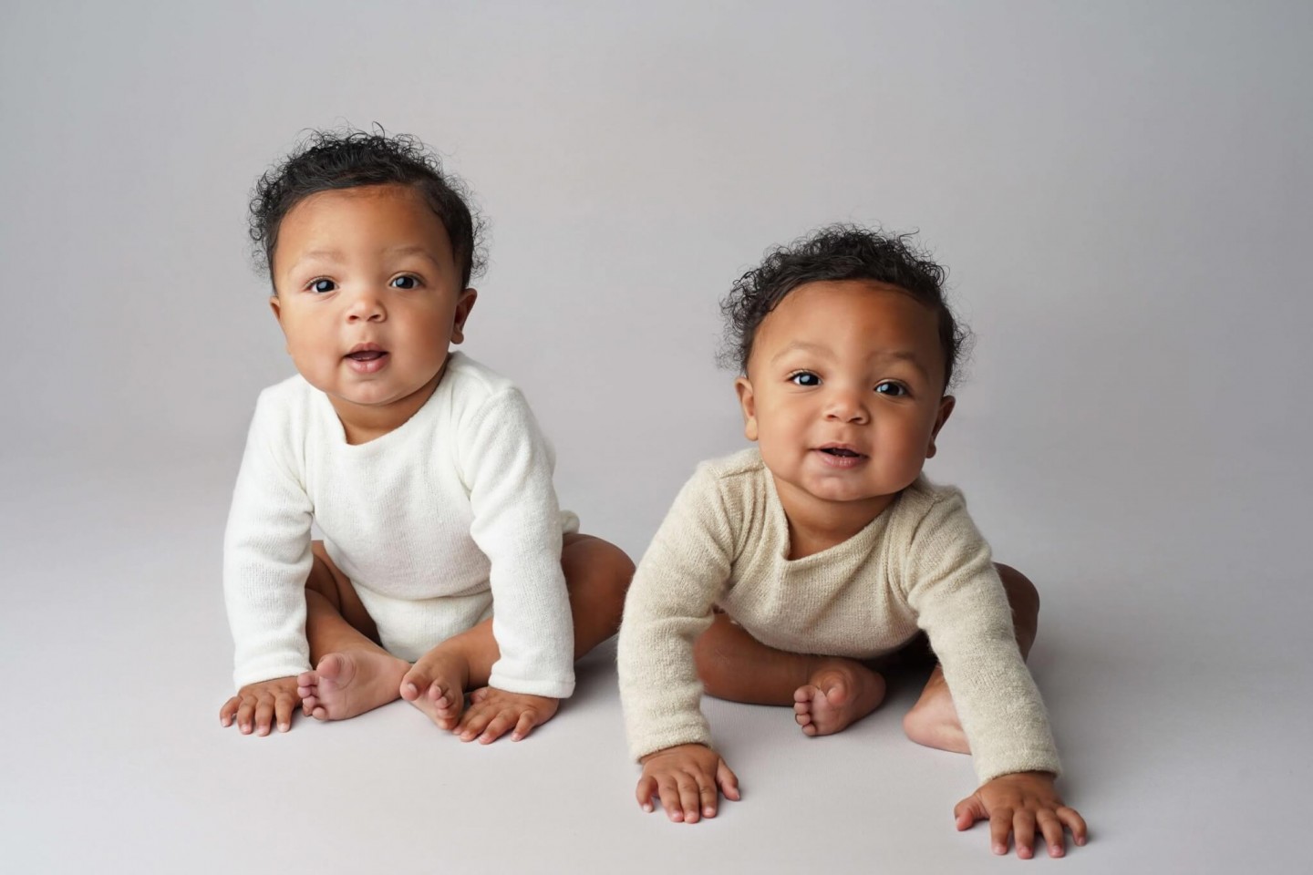 Two babies are sitting on a gray background.