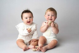 Two babies sitting on a white background.