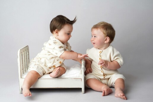 Two baby boys sitting on a wooden bed.