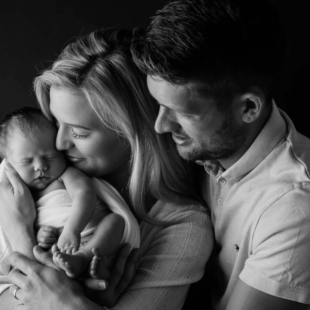 A black and white photo of a man and woman holding a newborn baby.