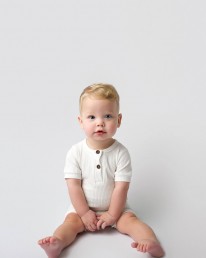 A baby in a white romper sitting on a white background.