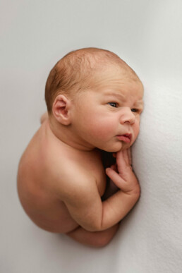 A newborn baby boy peacefully laying on a white background, captured in stunning newborn photography in Essex.