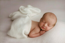 A newborn baby peacefully sleeping on a white blanket in Essex.