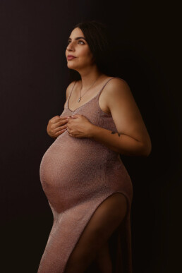 A pregnant woman in a pink dress posing against a black background.