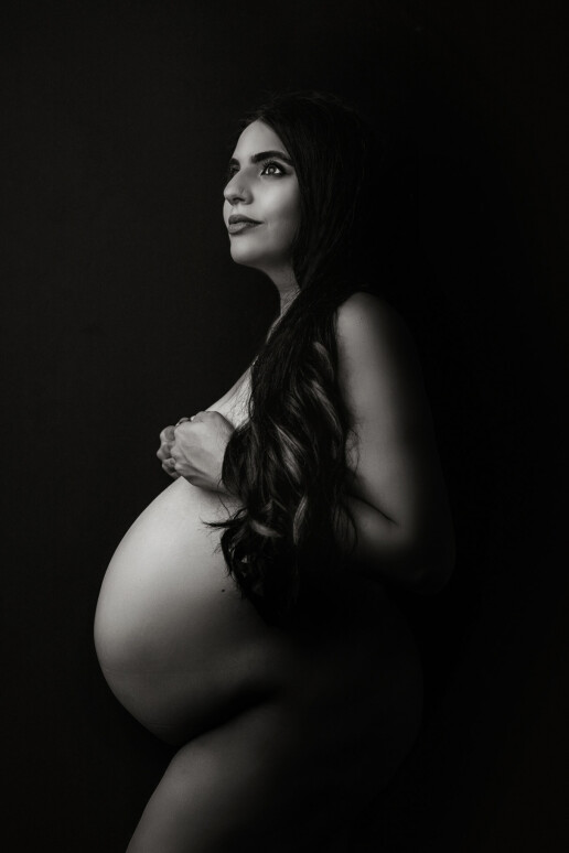 A pregnant woman is posing for a black and white photo.