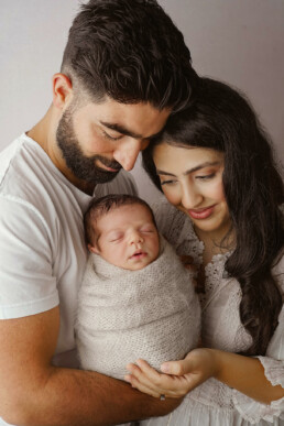 A couple is cradling a baby in a white blanket for their newborn photography session in Essex.