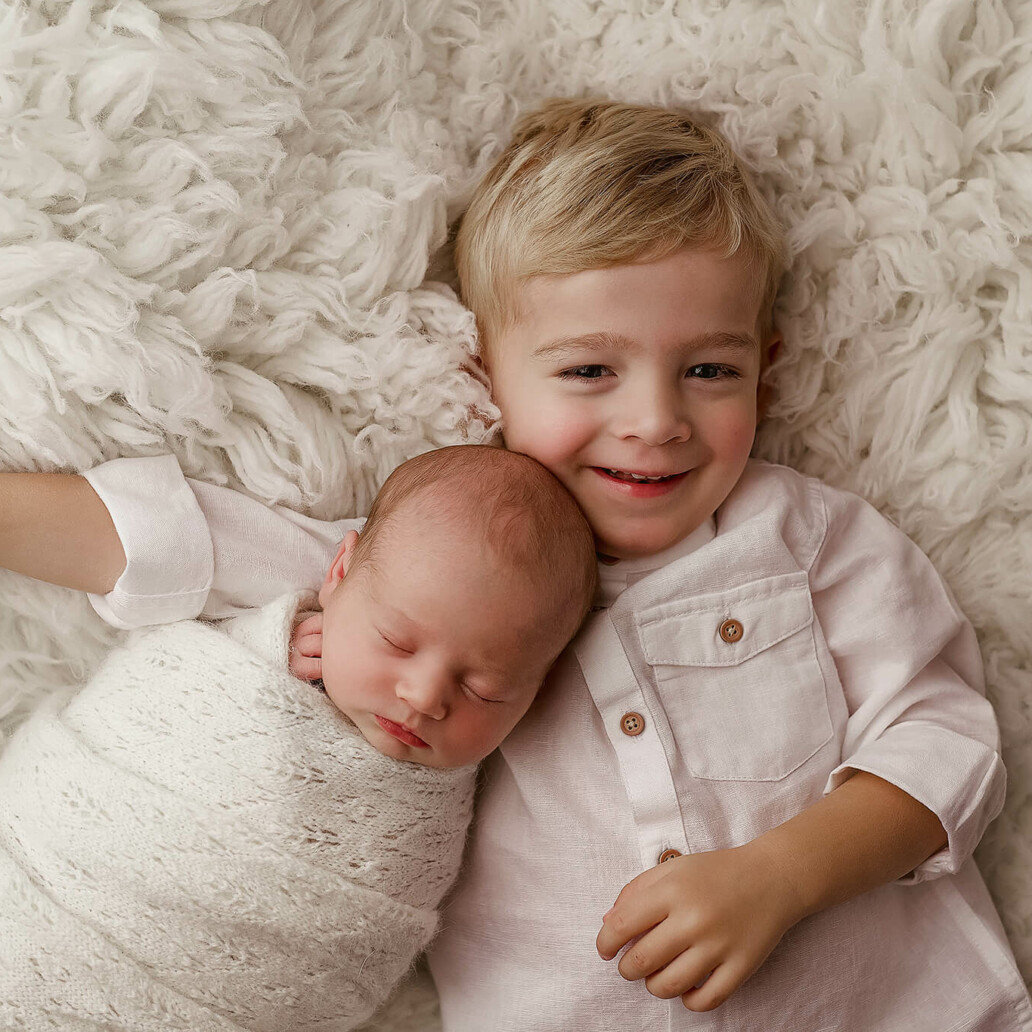 Two newborn boys laying on a white blanket.