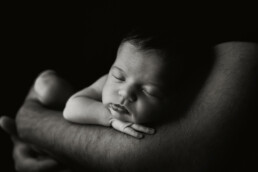 A black and white photo of a baby sleeping in his father's arms, perfect for newborn photography.