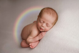 A newborn baby sleeping on a blanket with a rainbow in the background.