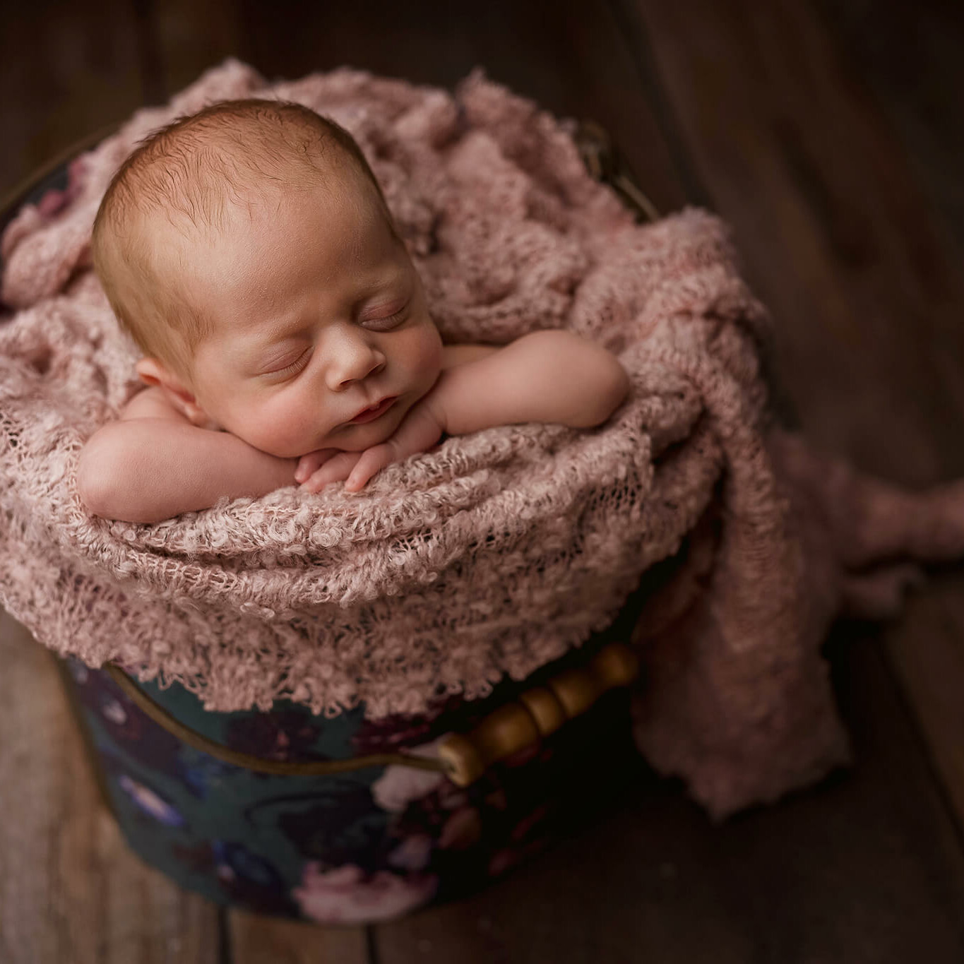 Capture stunning images of a newborn peacefully sleeping in a bucket on a wooden floor. Perfect for newborn photography in Essex.