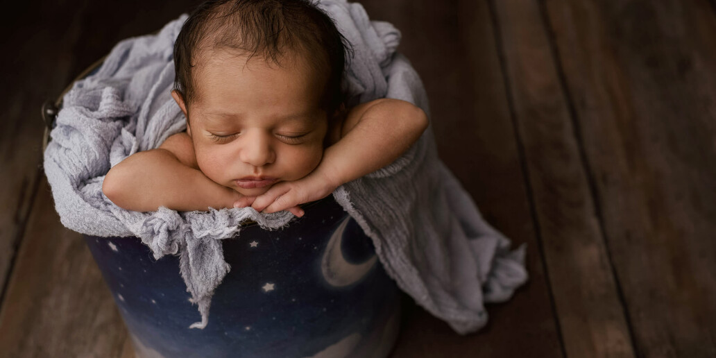 A newborn sleeping in a bucket on a wooden floor.