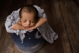 A newborn sleeping in a bucket on a wooden floor.
