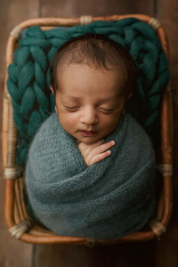 A newborn boy is swaddled in a blue blanket in a basket for Essex photography session.