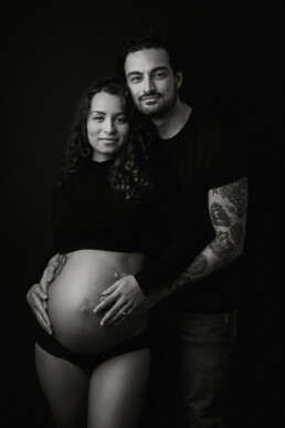 A pregnant couple posing for a black and white photo.