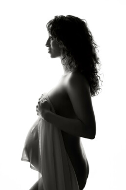 A pregnant woman is posing in front of a white background.