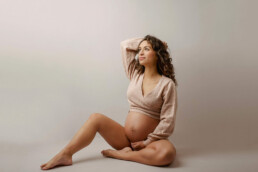 A pregnant woman posing on a gray background.