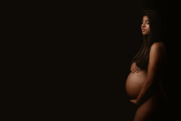 A pregnant woman posing on a dark background.