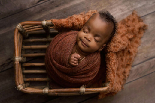 A baby boy sleeping in a basket on a wooden floor.