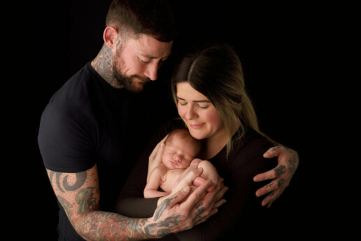 A man and woman holding a baby on a black background.