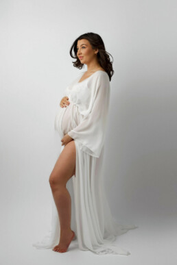 A pregnant woman in a white gown posing for a photo.