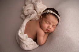 A baby sleeps on a soft surface with a white blanket and a headband.