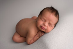 Newborn baby sleeping on stomach on a soft, light-colored surface.