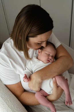 Woman in a white shirt cradles a sleeping baby dressed in white and pink tights, sitting on a light-colored chair—capturing a tender moment perfect for newborn photography Essex.
